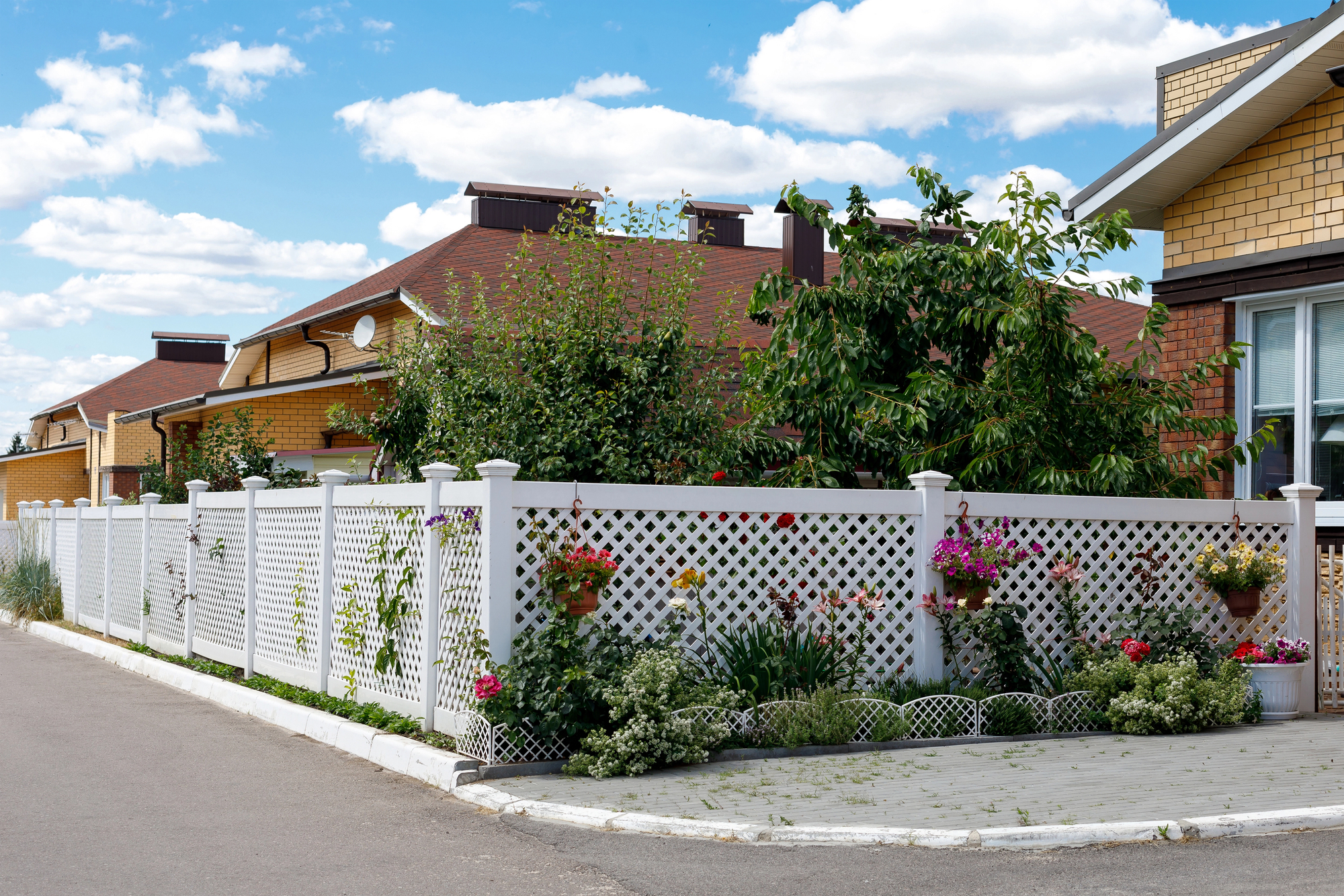 A house in a suburban cottage village with a white vinyl fence with ornamental plants and flowers in pots 